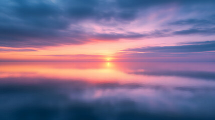 Fototapeta premium A colorful sunrise illuminating the horizon over a still mirror-like ocean surface.