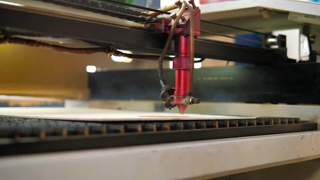 An industrial laser cuts a pattern on a sheet of plywood . Modern laser treatment of wood. A red laser beam passes through a tree. Laser cutting of engineered wood parts.