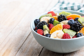 Fruit salad in a blue bowl on wooden table. Copy space