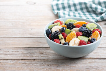 Fruit salad in a blue bowl on wooden table. Copy space