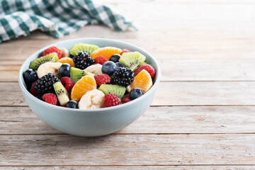 Fruit salad in a blue bowl on wooden table. Copy space