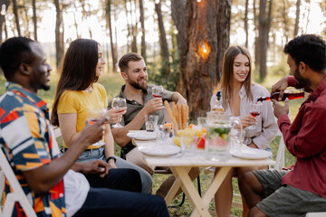 Meeting of multiracial group of friends eating dinner and drinking wine during party in the forest