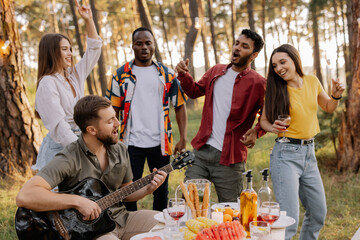 Multicultural group of people, bearded hipster man playing guitar and friends dancing and having fun