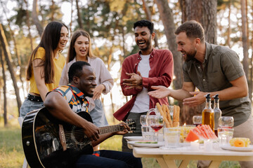 Multicultural group of people, African hipster man playing guitar and friends dancing, singing and having fun