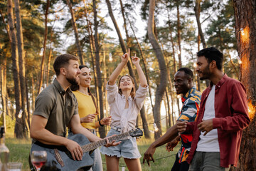 Multiracial group of people, bearded hipster man playing guitar and friends dancing, singing and having fun