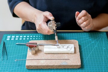 A woman in a studio works on jewelry using a gas torch to heat metal. Workplace of jeweler.