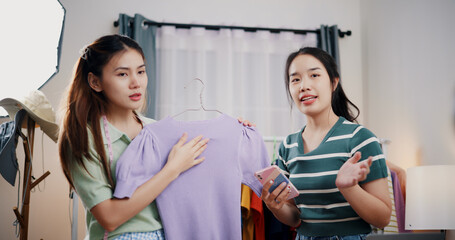 Obraz premium Portrait of Two cheerful woman influencers are live streaming sell clothes on social media or blogging in home studio. Remote buying, Online shopping, Sell ​​products online