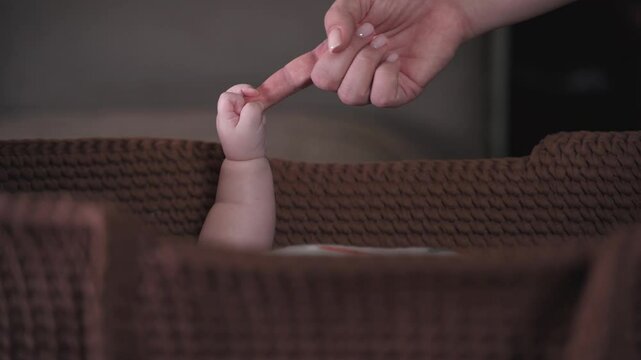 The baby's hand squeezes the mother's finger. Mother's tenderness, warmth and safe. The baby is in the crib