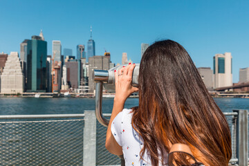 Tourist using binoculars admiring manhattan skyline from brooklyn heights promenade