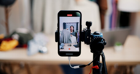 Selective focus on mobile phone of Cheerful woman influencer is live streaming sell clothes on social media or blogging in home studio. Remote buying, Online shopping, Sell ​​products online