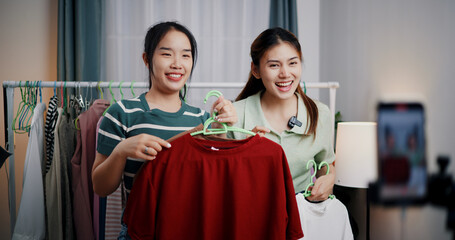 Portrait of Two cheerful woman influencers are live streaming sell clothes on social media or blogging in home studio. Remote buying, Online shopping, Sell ​​products online