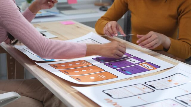 Two designers are moving cards representing different parts of a mobile application, discussing placement and user experience