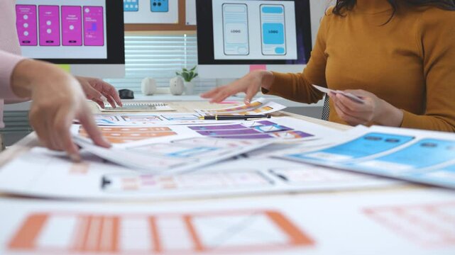 Two women working together in an office, moving cards on a table and discussing. They are designing a mobile application user interface