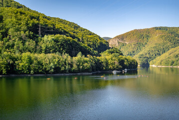 Fototapeta premium Serene Mountain Lake with Lush Green Forests, Kayakers and Canoeists in a Peaceful Natural Landscape - Summer Outdoor Adventure
