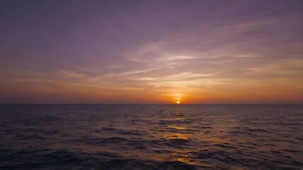 Obraz premium Sunset over the sea, showcasing a vibrant orange, red, and purple evening sky, with the ocean water gently rippling, providing a picturesque wallpaper background