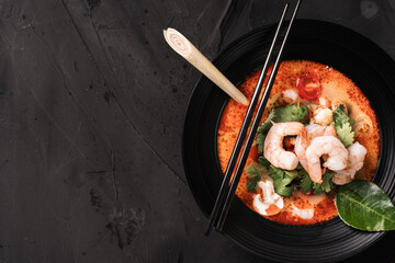 tom yum kung Spicy Thai soup with shrimp in a black bowl on a dark stone background, top view, copy space