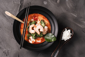 tom yum kung Spicy Thai soup with shrimp in a black bowl on a dark stone background, top view, copy...