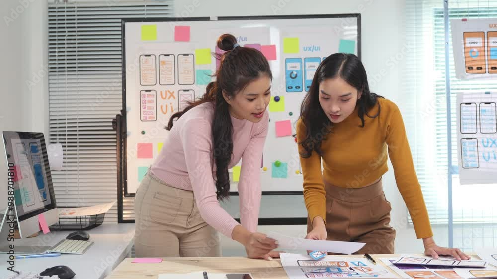 Poster two female web designers are discussing over design prototypes for a mobile application. they are st