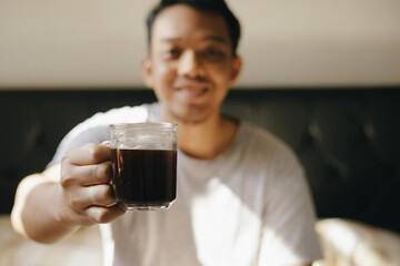 Asian man enjoy drinking coffee on the bed after wake up from sleep