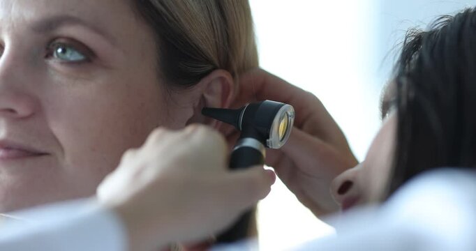 Woman doctor examines female patient ear using otoscope. Attentive medic in uniform checks organ searching for disease at appointment