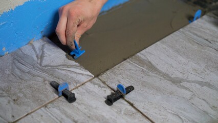 Construction worker placing tile leveling system while laying floor tiles.