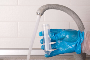 Analysis of tap water in the house, hand in blue glove draws water into a test tube from the tap...