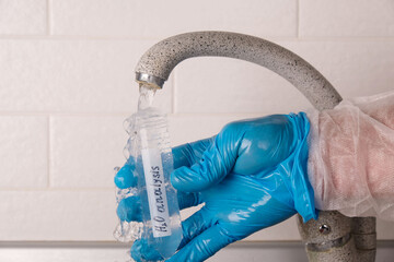 Analysis of tap water in the house, hand in blue glove draws water into a test tube from the tap...