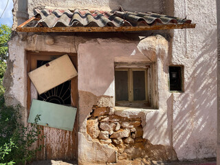 An old dilapidated house on modern street. Abandoned building ruins, damaged outer brickwall with aged crumbled plaster, broken windows and doors. Past and present of residential area, Athens, Greece.