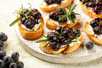 White board with Roasted Grape and Goat ricotta Cheese Crostini with rosemary. Fresh grape plant on the side.