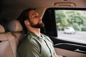 Man relaxing in a car with earbuds, eyes closed, enjoying music Soft interior colors create a calm atmosphere