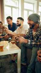 Close-up of pure joy as one player celebrates victory. Energy in room high, with drinks in hand and friends cheering each other on. Concept of football fans, sport evens, video games and cybersport.