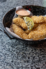 golden deep-fried battered chicken nuggets.succulent chicken chunks ensconced in a delectable batter, crisped up with Panko, and draped in sauce closeup on the plate on the table.