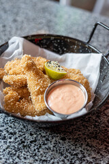 golden deep-fried battered chicken nuggets.succulent chicken chunks ensconced in a delectable batter, crisped up with Panko, and draped in sauce closeup on the plate on the table.