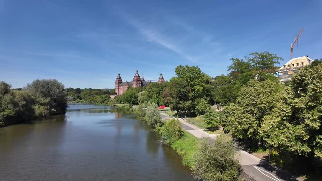 River Main in Aschaffenburg with distant towers of the castle Johannisburg, green recreational area with promenade, Bavaria, Germany