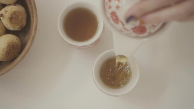 Top view of a person pouring tea into cups while a bowl of freshly baked chipa bread sits on the table, creating a cozy home traditional atmosphere