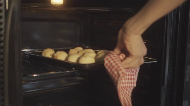 Person takes a tray of freshly baked chipa bread out of the oven, showcasing the home baking process of this traditional treat