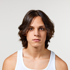 Portrait of young attractive man with long brunette hair and well-kept skin looking at camera calmly against white studio background. Concept of natural beauty, fashion, cosmetic product, male health.