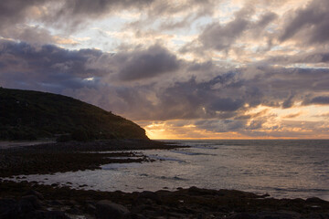 Dramatic sunset over rocky shore of Pacific Ocean near Raglan, New Zealand