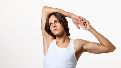 Calm young man stretching his hands and looking upwards against white studio background. Morning exercises. Concept of natural beauty, fashion, cosmetic product, male health. Ad