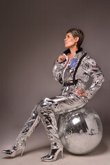 A businesswoman poses in a photo studio in a silver jumpsuit and a black stiletto dress.