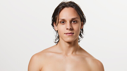 Obraz premium Portrait of young attractive brunette man with wet hair posing shirtless against white studio background. Concept of natural beauty, fashion, cosmetic product, male health. Ad