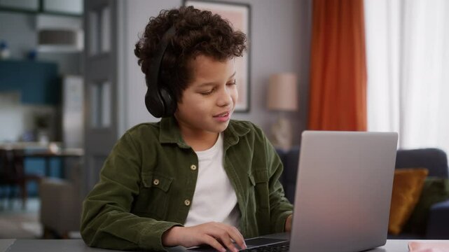African American son kid child boy in headphone at home typing browsing laptop playing video game computer distant play gaming online internet addiction win celebrate success achieve victory winning