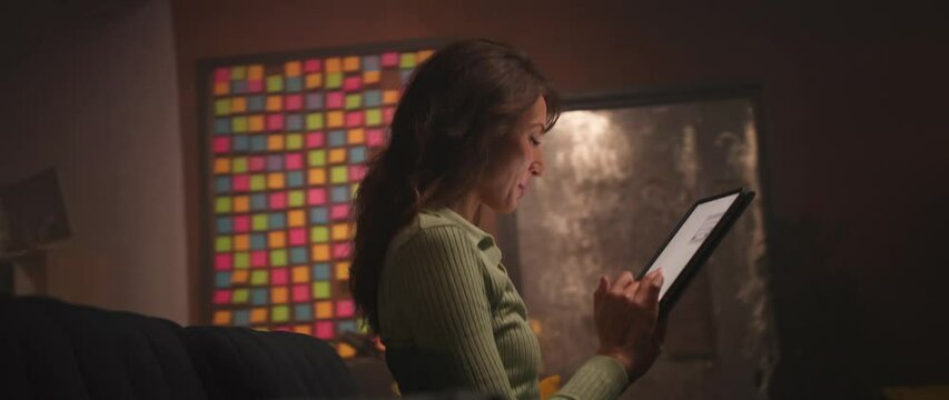360 degree time-lapse home. Young focused Caucasian woman holding digital tablet and scrolling through social media feed, reading messages, chatting at home. Smiling girl using gadget in evening
