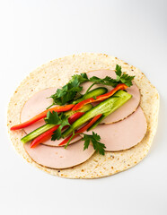 Fresh tortilla wrap preparation with turkey slices, vibrant peppers, and cilantro on a clean surface