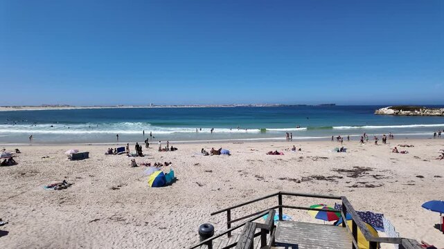 View of Baleal Sul Beach in Peniche, Portugal, showcasing sandy shores, blue waters, and beachgoers under a bright sky.
