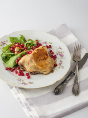 A beautifully plated chicken dish garnished with pomegranate seeds and fresh greens on a vintage floral plate