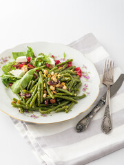 Delightful green bean salad with fresh greens and pomegranate, beautifully plated on vintage china, perfect for a festive meal or gathering