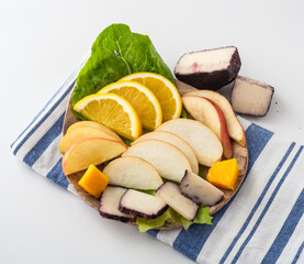 Colorful fruit platter featuring fresh slices of apple, orange, and exotic tropical fruits on a wooden plate with leafy greens