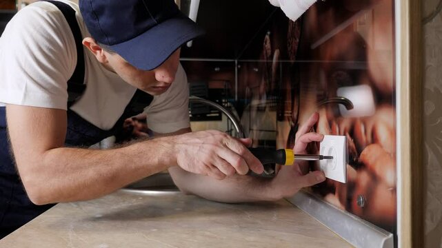 Close-up of an electrician installing or repairing an outlet in the kitchen in an apartment.