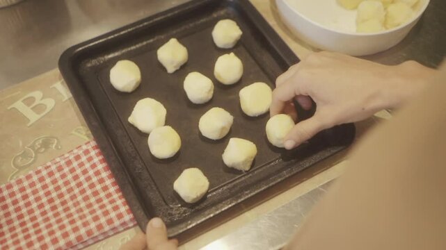 Hands carefully placing raw chipa dough balls on a baking tray, capturing the process of making traditional hallowed bread at home